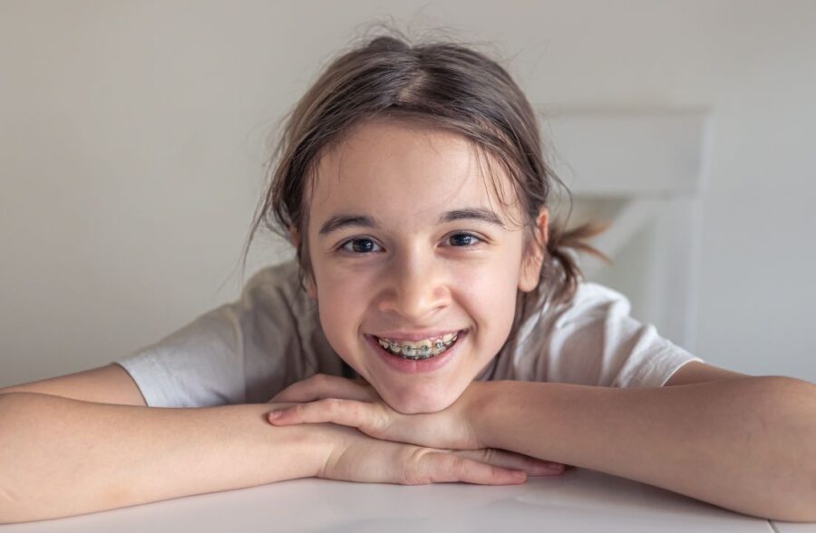 A smiling child with braces on their teeth, representing the importance of early orthodontic treatment for crooked teeth in kids