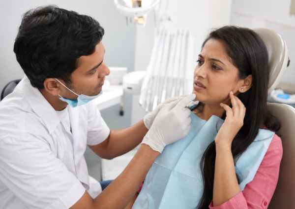 Indian woman discussing jaw discomfort with a dentist during a dental implant check-up inside a modern dental clinic.