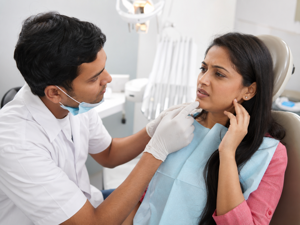 Indian woman discussing jaw discomfort with a dentist during a dental implant check-up inside a modern dental clinic.